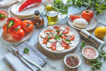 Caprese salad with sliced fresh tomatoes, mozzarella cheese and basil served on a white plate on...