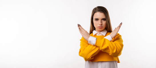 Serious Young brunette woman keeps two arms crossed, makes stop or ban gesture. Studio shot, white...