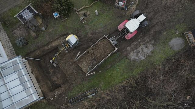 aerial drone shot of yellow excavator stands in a large garden and digs a hole for a pool in austria