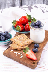 Healthy breakfast with homemade yoghurt and fresh strawberries and blueberries, crispbread on a white wooden table in rustic style, close up, vertical.