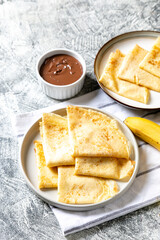 Crepes, thin pancakes on a plate. Chocolate hazelnut spread and banana filled crepes on plate. Tasty crepes or blini with sweet sauce