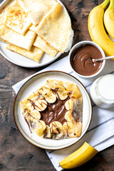 Crepes, thin pancakes on a plate. Chocolate hazelnut spread and banana filled crepes on plate. Tasty crepes or blini with sweet sauce