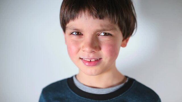 Portrait of a child on a white background. The boy squints his eyes, looks at the camera. The emotion of embarrassment.