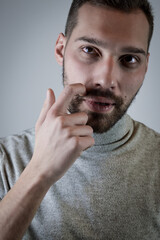 Portrait of a young man scratching his beard with a finger while he is thinking about something