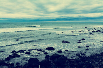 Retro-style photo of dark stormy day at Pacific ocean. Rip tide breaking at black rocks of the surf. Cape Egmont, New Zealand