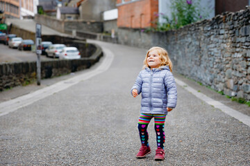 Beautiful portrait of cute little toddler girl. Happy baby child looking at the camera and smiling. Kid making a walk through historical old town. Outdoors at the dusk.