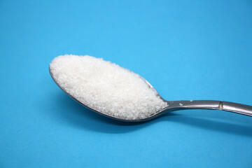 Sugar poured into a spoon on a blue background.