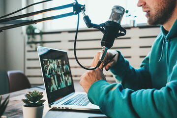 Cheerful man host streaming his live podcast using microphone and laptop at his homemade  broadcast...