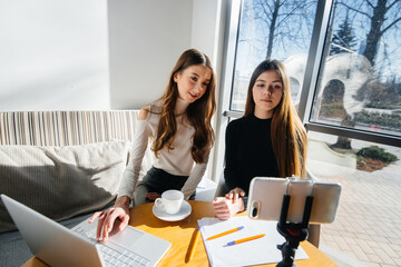 Two young beautiful girls are sitting in a cafe, recording video blogs and communicating on social networks.