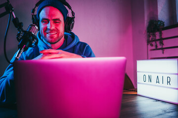 Trendy podcast creator streaming live audio show at his home studio using stylish cyber punk...