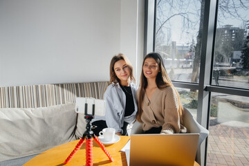 Two young beautiful girls are sitting in a cafe, recording video blogs and communicating on social networks.