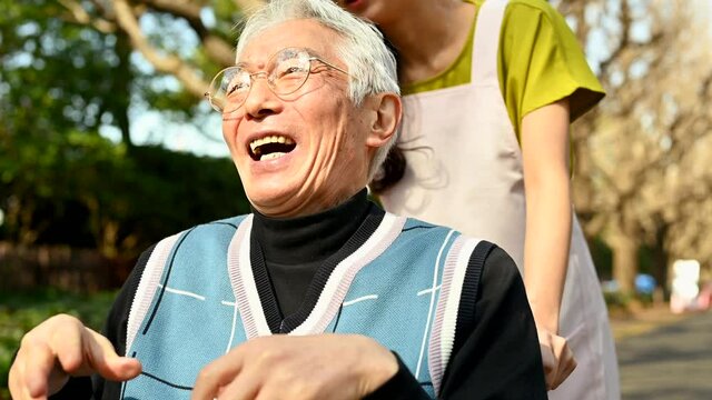 楽しそうに外を散歩する車椅子に乗った高齢者と女性福祉士	
