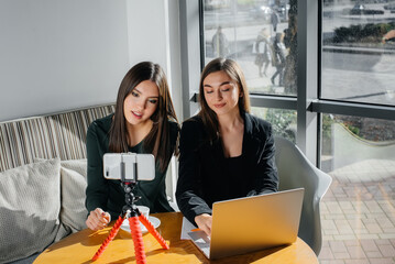 Two young beautiful girls are sitting in a cafe, recording video blogs and communicating on social networks.