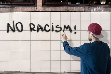 person male write with spray paint can the stop no racism  statement on the wall, graffiti symbol...