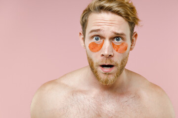 Close up shocked worried bearded naked young man 20s perfect skin wearing moisturizing patches under eyes isolated on pink background studio portrait. Skin care healthcare cosmetic procedures concept.