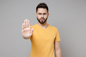 Young caucasian serious strict bearded pensive handsome man in casual yellow basic t-shirt sctratch...