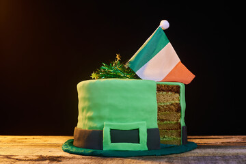 green frosting cake shaped like a green hat with an Irish flag on top, to celebrate St. Patrick's Day. Natural wood base