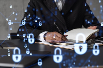 Businesswoman is taking notes of clients needs to protect cyber security from hacker attacks and save clients confidential data. Padlock Hologram icons over the typing hands. Formal wear