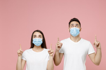 Young couple two friends man woman in white blank print design tshirts sterile face mask to safe from coronavirus virus covid19 on quarantine posing isolated on pastel pink background studio portrait