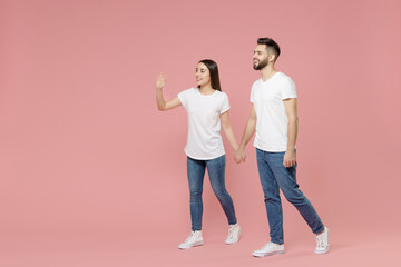 Fototapeta premium Full body length side profile view young lovely couple two friends man woman in white basic blank print design t-shirt jeans walk go move step isolated on pastel pink color background studio portrait.