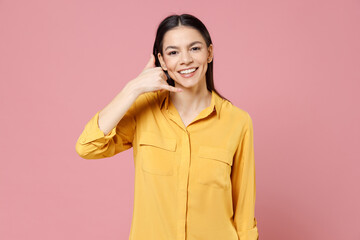 Fototapeta premium Young positive happy friendly brunette attractive latin woman 20s wear yellow casual shirt doing phone gesture like says call me back look camera isolated on pastel pink background studio portrait