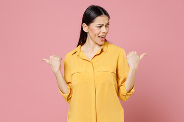 Young brunette confused surprised happy cute latin happy attractive cute woman 20s in yellow shirt point hands aside on copy space area mock up isolated on pastel pink background studio portrait