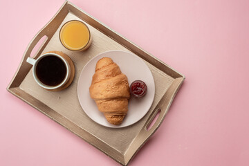 On a pink background a tray with breakfast. On a tray hot coffee, delicious croissant, orange juice. Breakfast in bed.