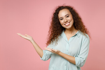 Young black african american smiling happy curly woman 20s wearing blue shirt point hands arms...