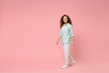 Fototapeta na wymiar Full length young black african american happy smiling positive friendly curly woman 20s in blue casual shirt looking camera walking going strolling isolated on pastel pink background studio portrait.