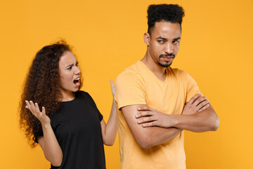 Young couple friends together family african indignant angry woman man 20s in black tshirt scream shout arguing with boyfriend hands folded crossed isolated on yellow color background studio portrait