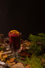 hot mulled wine drink in a glass against the background of spruce branches and dry leaves. New Year's festive mood. High quality photo