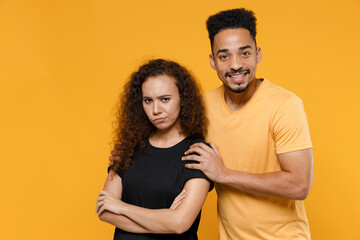 Young couple friends together family african frowning resentful woman man 20s in black yellow tshirt hug offended girlfriend reconciling apologizes isolated on orange color background studio portrait