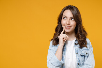 Young caucasian smiling dreamful wistful brunette woman in stylish casual denim shirt white t-shirt show prop up chin look aside isolated on yellow background studio portrait People lifestyle concept.