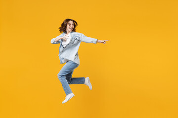 Fototapeta na wymiar Full length of young excited fun expressive student woman 20s wearing denim shirt white t-shirt run jump high point index finger aside on workspace area isolated on yellow background studio portrait