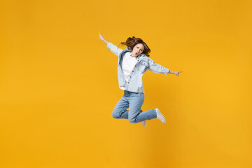 Fototapeta na wymiar Full length of young overjoyed excited fun expressive student happy woman 20s wear denim shirt white t-shirt with outstretched hands legs jumping high isolated on yellow background studio portrait