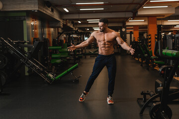 Fototapeta na wymiar a male athlete with a naked torso, abs and pumped-up muscles stands in the gym with his arms spread out to the side. High quality photo