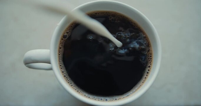 Pouring milk in coffe in cafe top view, super slow motion