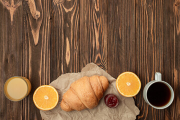 On a wooden background, fresh croissants, orange juice, oranges, hot coffee. Delicious breakfast concept. Place for text.