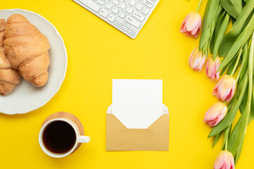 An envelope with a postcard is arranged on a yellow background and pink tulips. Spring concept, mother's day, women's day