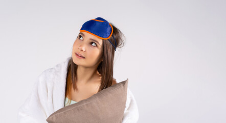 Banner, long format. An attractive girl in a cozy pajamas and a blindfold with a pillow in her hands looks up thoughtfully. White background and side advertising space.