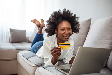 Shot of a young woman using a laptop and credit card while relaxing at home. Keeping the shopping mall close to home. Shopping spree directly from the sofa