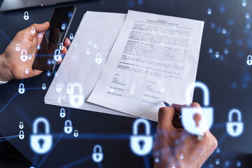 A businessman in formal wear signing the contract to prevent probability of risks in cyber security. Padlock Hologram icons over the working desk.