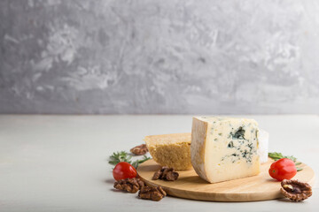 Blue cheese and various types of cheese with rosemary and tomatoes on wooden board on a white and gray background . Side view, copy space.