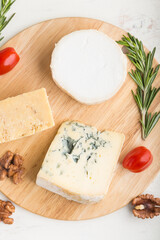 Blue cheese and various types of cheese with rosemary and tomatoes on wooden board on a white background . Top view.