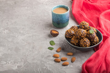 Chocolate caramel ball candies with almonds and a cup of coffee on a gray concrete background and red textile. Side view, copy space.