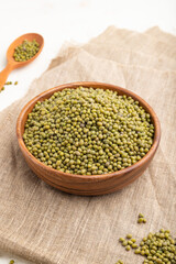 Wooden bowl with raw green mung bean and wooden spoon on a white  background. Side view, close up.