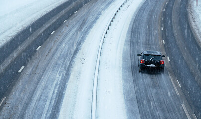 Cars driving on a highway in a blizzard with the road covered in snow and ice on a cold winters day.