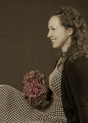 Portrait of young beautiful smiling woman with bouquet of rose flowers. Pink color in roses. Sitting in a dress and curly hair. In brown vintage photo colors. Vintage, retro style from 1900