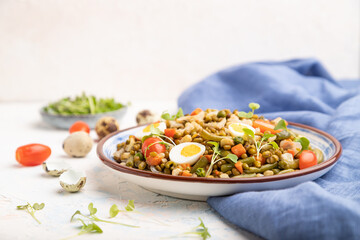 Mung bean porridge with quail eggs, tomatoes and microgreen sprouts on a white concrete background. Side view, selective focus, copy space.