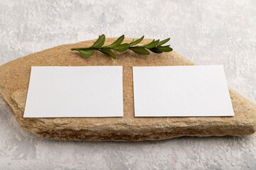 White paper business card, mockup with stone and boxwood branch on gray concrete background. side view, copy space.
